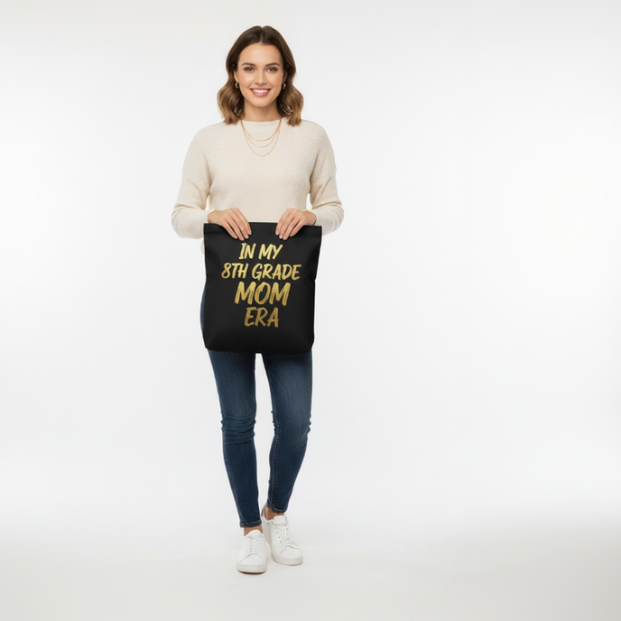 Woman holding black Class of 2027 8th Grade Mom Era tote bag for school fundraiser