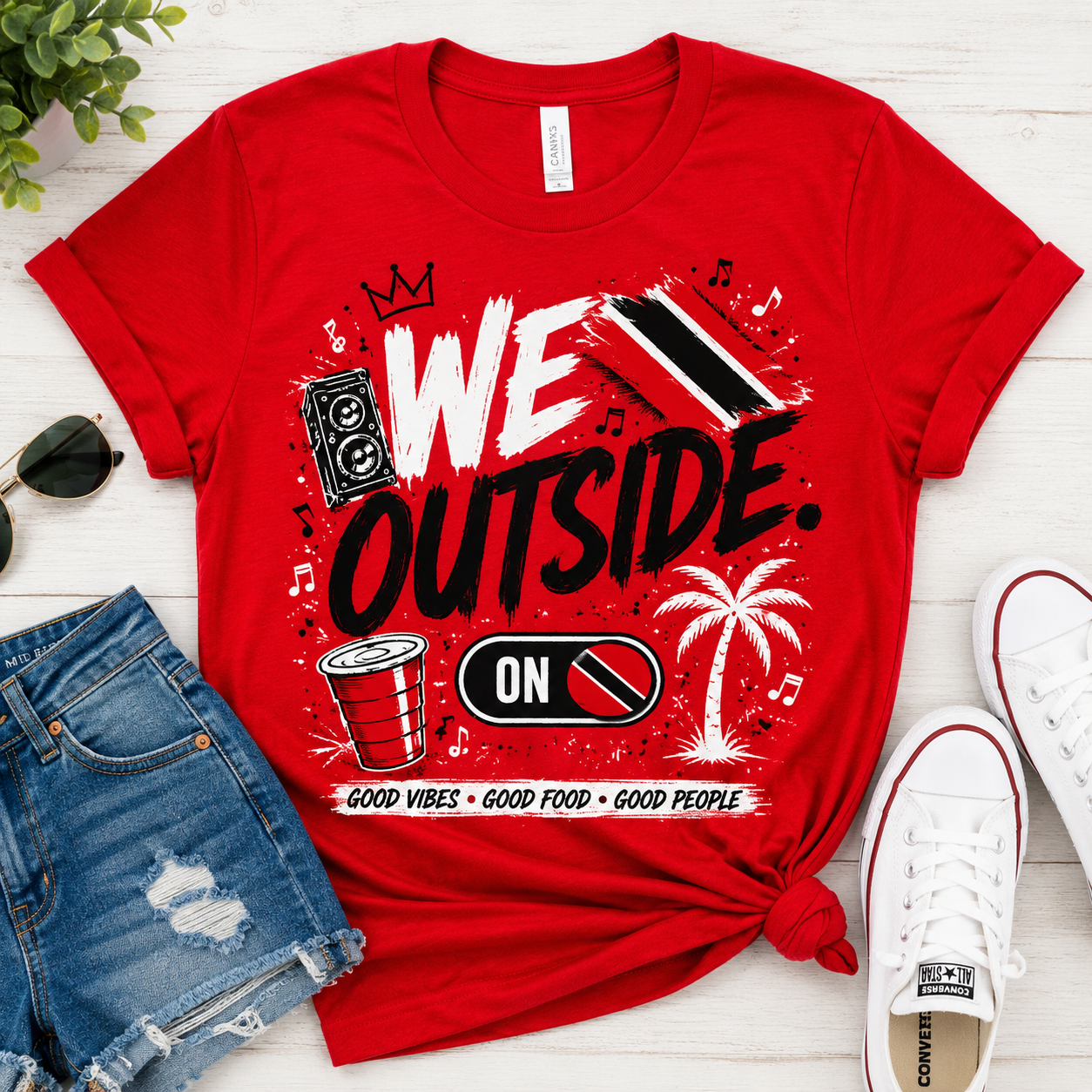 We Outside Trinidad and Tobago graphic tee in red with black and white design, flat lay with denim shorts and white sneakers