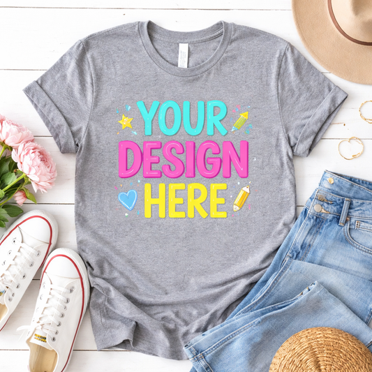 Gray custom t-shirt mockup with ‘Your Design Here’ text, shown flat lay with jeans and sneakers